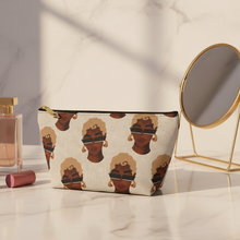 Load image into Gallery viewer, A cosmetic pouch with a repeating illustrated face pattern sits on a marble surface beside makeup brushes, a perfume bottle, lipstick, and a small round mirror.