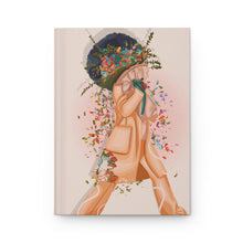 Load image into Gallery viewer, A matte hardcover journal with a floral-themed illustration on the cover, featuring a stylized female figure adorned with a colorful umbrella and surrounded by various flowers.
