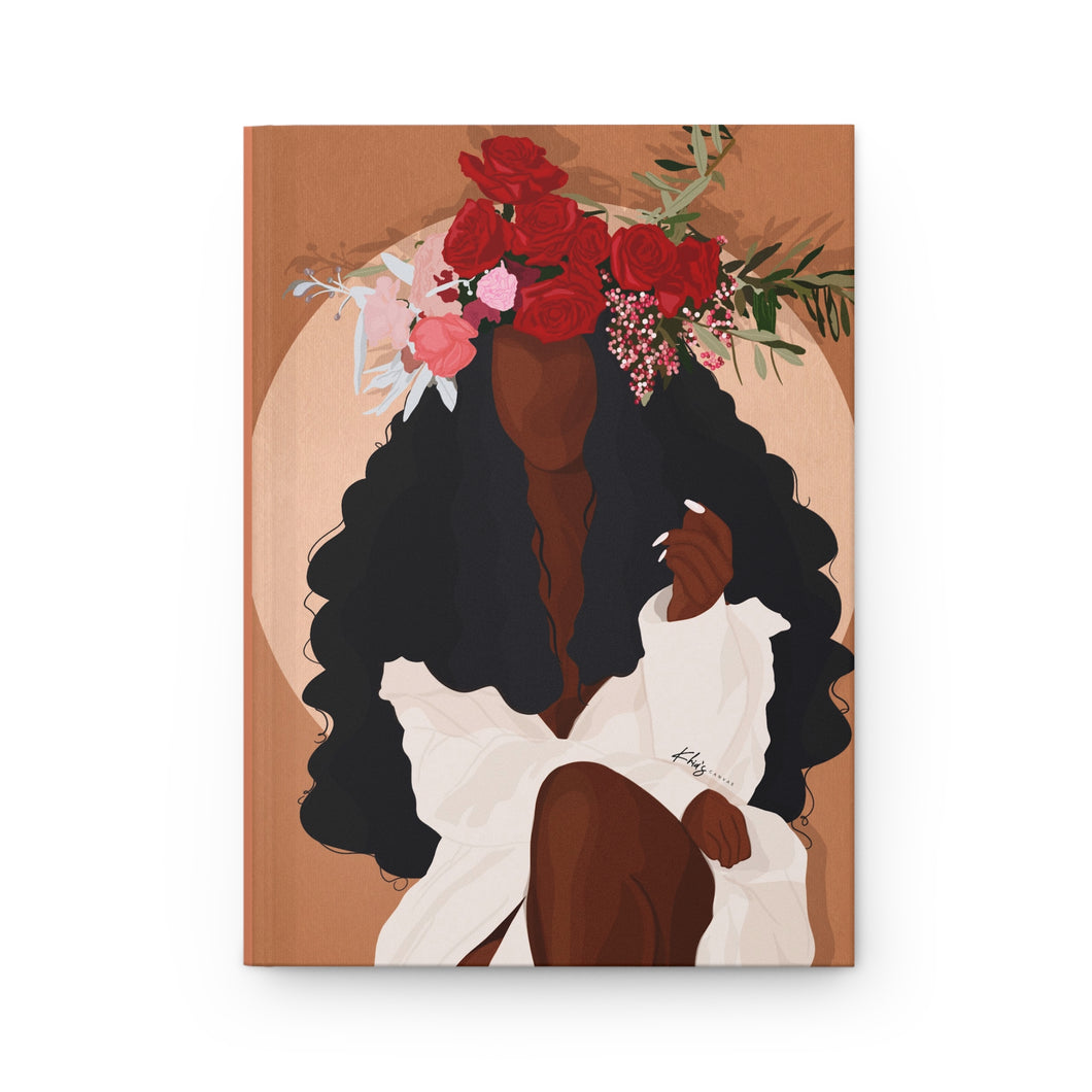 A matte hardcover journal with a cover illustration of a woman with a floral headdress and a dress, sitting in a contemplative pose.