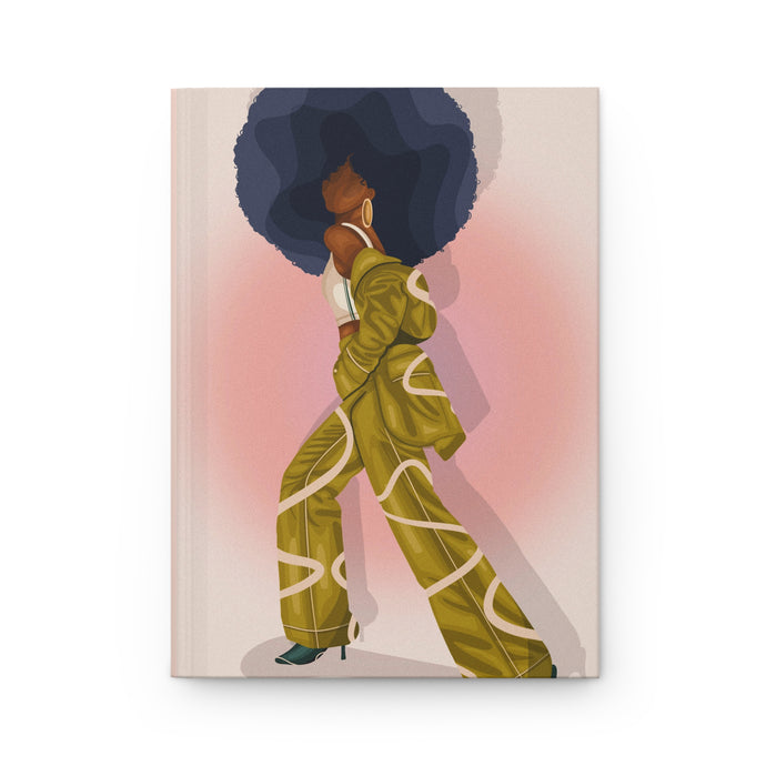 A matte hardcover journal with a cover illustration of a person with a large afro wearing a yellow and patterned outfit.